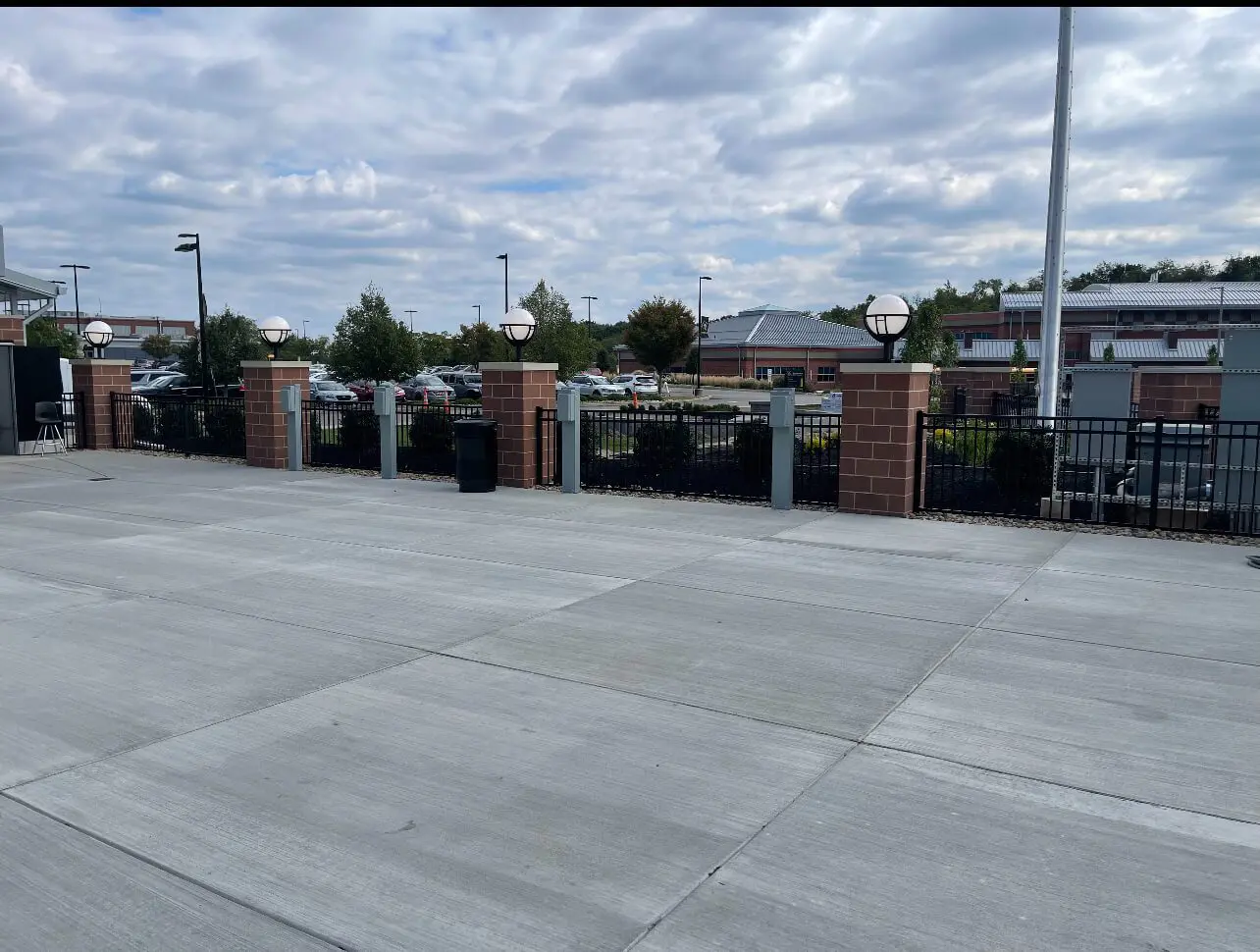 A parking lot with a fence and trash cans.